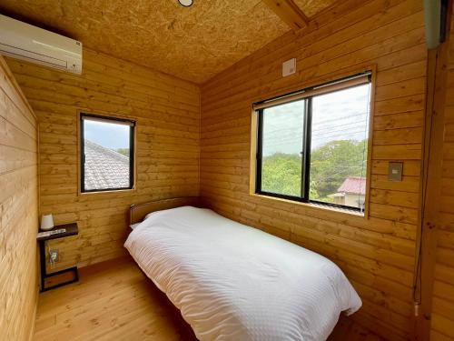 a bed in a wooden room with two windows at Kujukuri SOSA -九十九里 海辺のコテージ SOSA- in Sosa