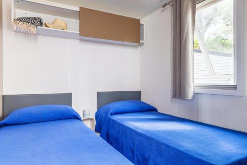 two beds in a room with blue sheets and a window at Gitavillage Le Marze in Marina di Grosseto