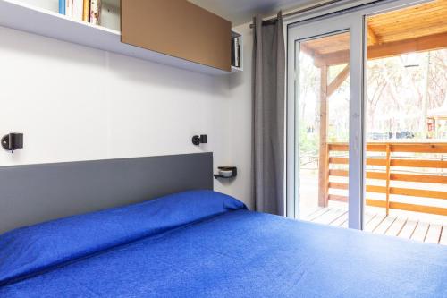 a bedroom with a blue bed and a sliding glass door at Gitavillage Le Marze in Marina di Grosseto
