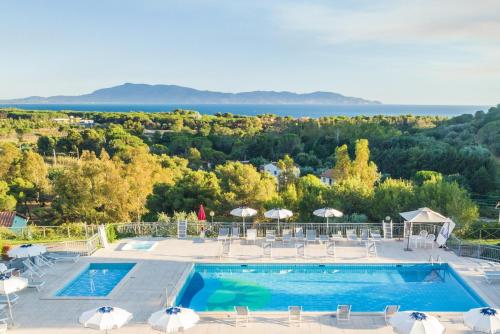 a pool with chairs and umbrellas and the ocean at Argentario Osa Resort in Talamone