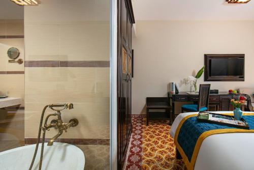 a bathroom with a tub and a bed and a television at La Charm Hoi An Hotel & Spa in Hoi An