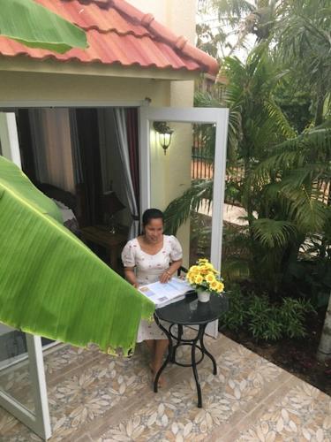 a woman sitting at a table in front of a house at B&B Verger Vannary in Phumĭ Băk Chĕnhchiĕn