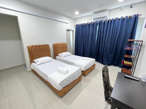 two beds in a room with blue curtains and a desk at TAMU ROOMSTAY TOK MOLOR in Kuala Terengganu