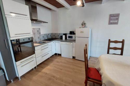 una pequeña cocina con armarios blancos y nevera. en Gîte pour 6 pers avec jardin clos proche Aurillac, 