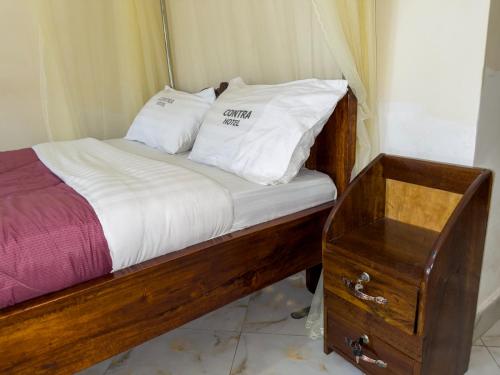 uma cama com duas almofadas brancas e uma mesa de madeira em Contra Hotel em Jinja