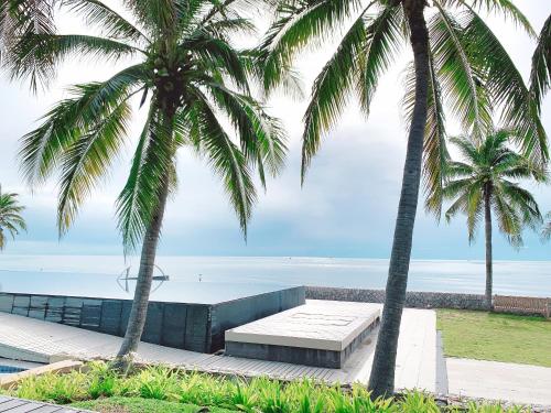 two palm trees and a bench in front of the ocean at Villa Nilaya - Beachfront Villa - Hua Hin in Ban Bo Fai