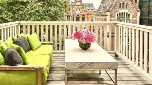 a couch and a table on a balcony with a vase of flowers at Conservatorium Hotel in Amsterdam