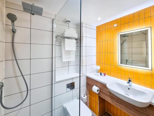 ein Bad mit einer Dusche, einem Waschbecken und einem Spiegel in der Unterkunft Cedar Court Hotel Huddersfield in Huddersfield