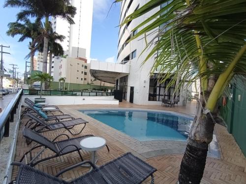 a swimming pool with chairs and a palm tree at Natal Plaza requinte, conforto e vista para o mar in Natal