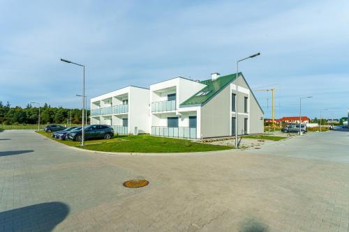 een wit huis met een auto geparkeerd op een parkeerplaats bij Sunset Resort IV, Nadmorska 98B in Grzybowo