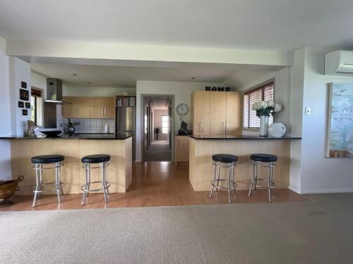a kitchen with three bar stools and a counter at Secluded Bays Home in Auckland