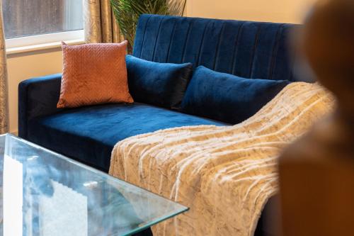ein blaues Sofa mit orangefarbenem Kissen neben einem Glastisch in der Unterkunft Watford Casa - 2 bed and 2 bath home near Watford Junction Station in Watford