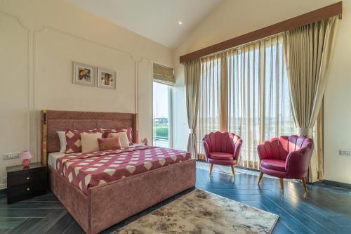 a bedroom with a bed and two pink chairs at StayVista at Serenity Farms with Pool, Lawn, Bonfire & BBQ in Sohna