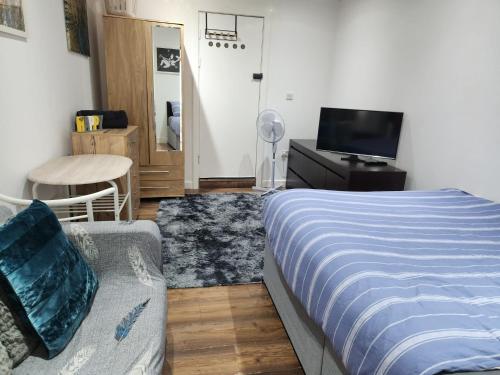 a bedroom with a bed and a couch and a tv at Studio Apartment at Chadwell Heath in Romford