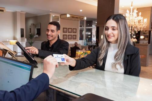 a woman sitting at a counter holding a credit card at Hotel Dan Inn Araraquara by Nacional Inn in Araraquara