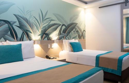 two beds in a hotel room with a tropical wallpaper at Portobelo Plaza de las Americas in San Andrés
