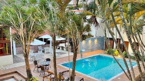 uma piscina com palmeiras, uma mesa e cadeiras em Pousada Estalagem dos Corais da Prainha em Arraial do Cabo
