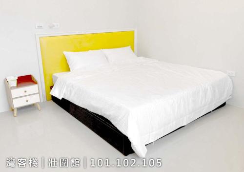 1 dormitorio con 1 cama blanca grande y mesita de noche en 灣客棧壯圍56館 en Yilan City