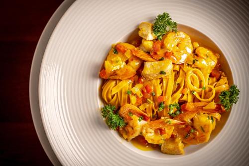 a white plate of pasta with chicken and vegetables at Porto Pacuíba Hotel in Ilhabela