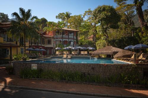 a swimming pool with chairs and umbrellas in front of a building at Porto Pacuíba Hotel in Ilhabela