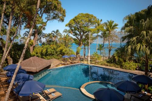 a swimming pool with umbrellas and chairs and the ocean at Porto Pacuíba Hotel in Ilhabela