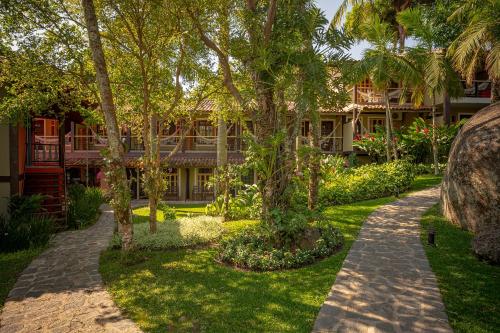 a garden with trees and a building in the background at Porto Pacuíba Hotel in Ilhabela