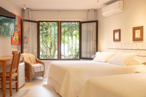 a bedroom with two beds and a desk and a window at Porto Pacuíba Hotel in Ilhabela
