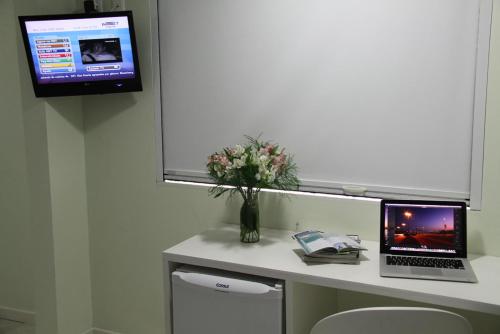 a desk with a laptop computer and a vase of flowers at Hotel Don Zepe in Florianópolis