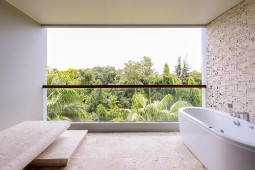 un bagno con vasca bianca e una grande finestra di The Regent Bangtao Apartments gorgeous view of the jungle a Bang Tao Beach