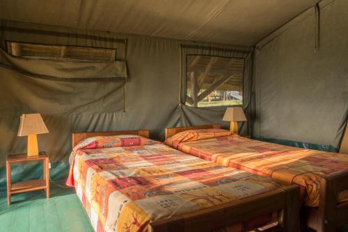 a bedroom with two beds and a table with a lamp at Bwana Tembo Safari Camp in Paraa