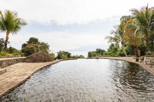 un bassin d'eau avec des palmiers en arrière-plan dans l'établissement Ilhabela Chalés, à Ilhabela