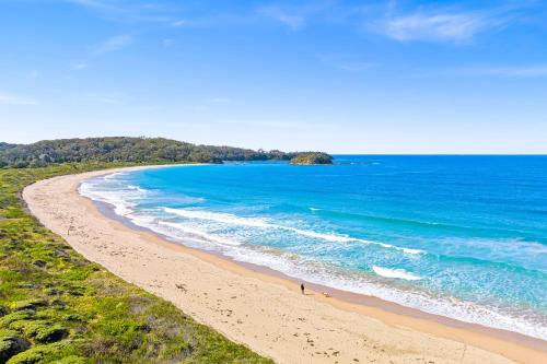 a beach with blue water and a person walking on it at Barlings Beach Holiday Park in Tomakin