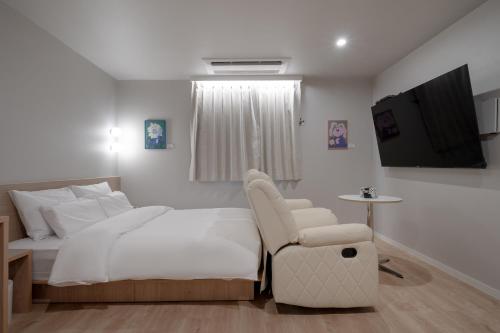 a white bedroom with a bed and a chair at Cheonan Aank Hotel Seongjeong in Cheonan