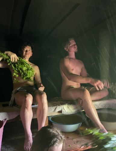 two men sitting on beds in a tent with vegetables at Wiire old fishermans farmhouse and smoke sauna in Saulepa