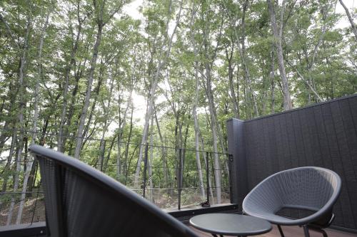 a balcony with two chairs and a view of trees at SAUNA FOREST CABIN 軽井沢 御代田 A棟 zen-asobi in Oiwake