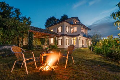 two chairs sitting around a fire in front of a house at SaffronStays The Clairmont Cottage,Mukteshwar in Mukteshwar