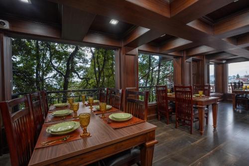 uma sala de jantar com mesa, cadeiras e janelas em The West Gate Posada By Summit em Darjeeling