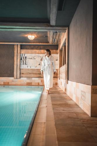 a woman in a white dress standing next to a swimming pool at Alpin Juwel - Bio und Lifestylehotel in Saalbach Hinterglemm