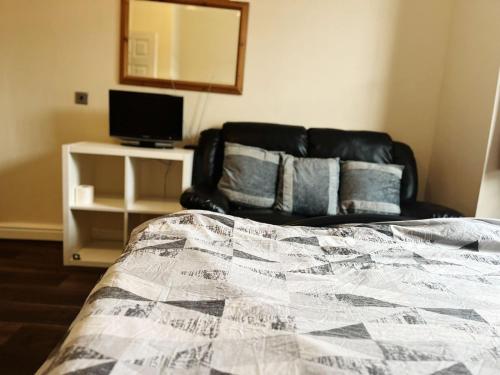 a bedroom with a bed and a black leather couch at Nice and Pleasant in Thornton Heath