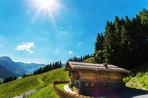 a wooden building on a hill with the sun in the sky at Schönwieshütte in Saalbach-Hinterglemm