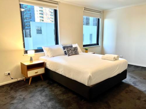 a bedroom with a large bed and two windows at ReadySet Apartments on Kavanagh in Melbourne