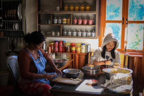 dos mujeres sentadas en una mesa preparando comida en Wake In Himalayas, en Pelling