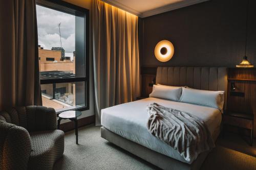 a bedroom with a bed and a chair and a window at Hotel Pinar Plaza in Madrid