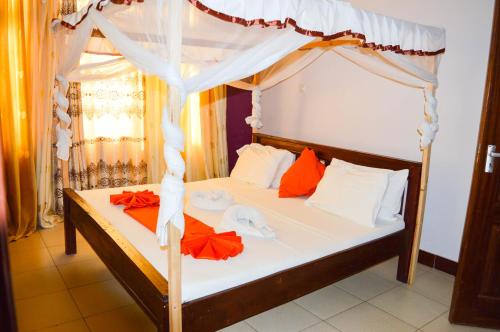 a bedroom with a canopy bed with orange and white pillows at Roma Stays - Elegant Apartment at Sunset Paradise with Swimming Pool & Restaurant in Mombasa