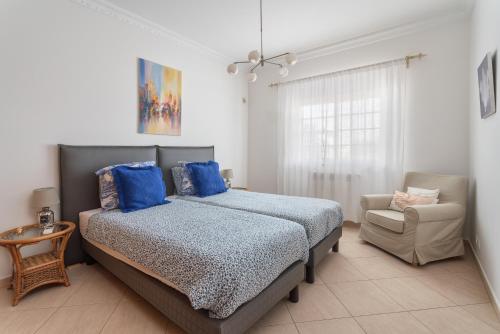 a bedroom with a bed with blue pillows and a chair at Fonte Santa Villa in Quarteira