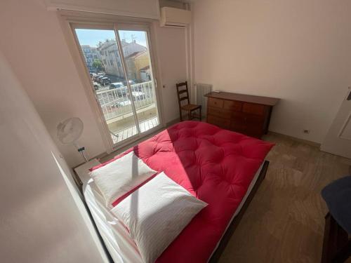 Schlafzimmer mit einem roten Bett und einem Fenster in der Unterkunft 2 piéces bord de mer à proximité nice, antibes et monaco, 4 personnes à cros de cagnes sur mer in Cros-de-Cagnes