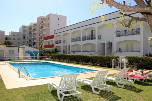 a swimming pool with two lawn chairs and a building at Apartamentos King's in Quarteira