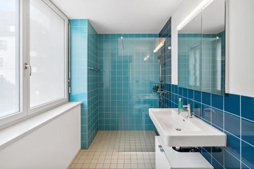 ein blau gefliestes Bad mit einem Waschbecken und einem Spiegel in der Unterkunft Zurich Flat: Central & Lake Convenience in Zürich