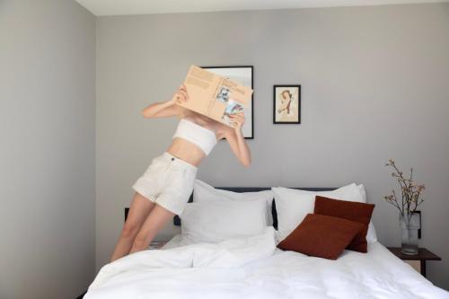 a woman is jumping on a bed with a book at Bob W Amsterdam Noord in Amsterdam