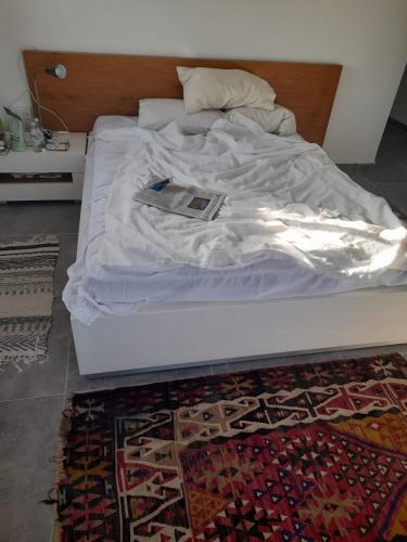 a white bed with a book on it on a rug at דירה נעימה בבנין הקהילתי הירוק in Harish